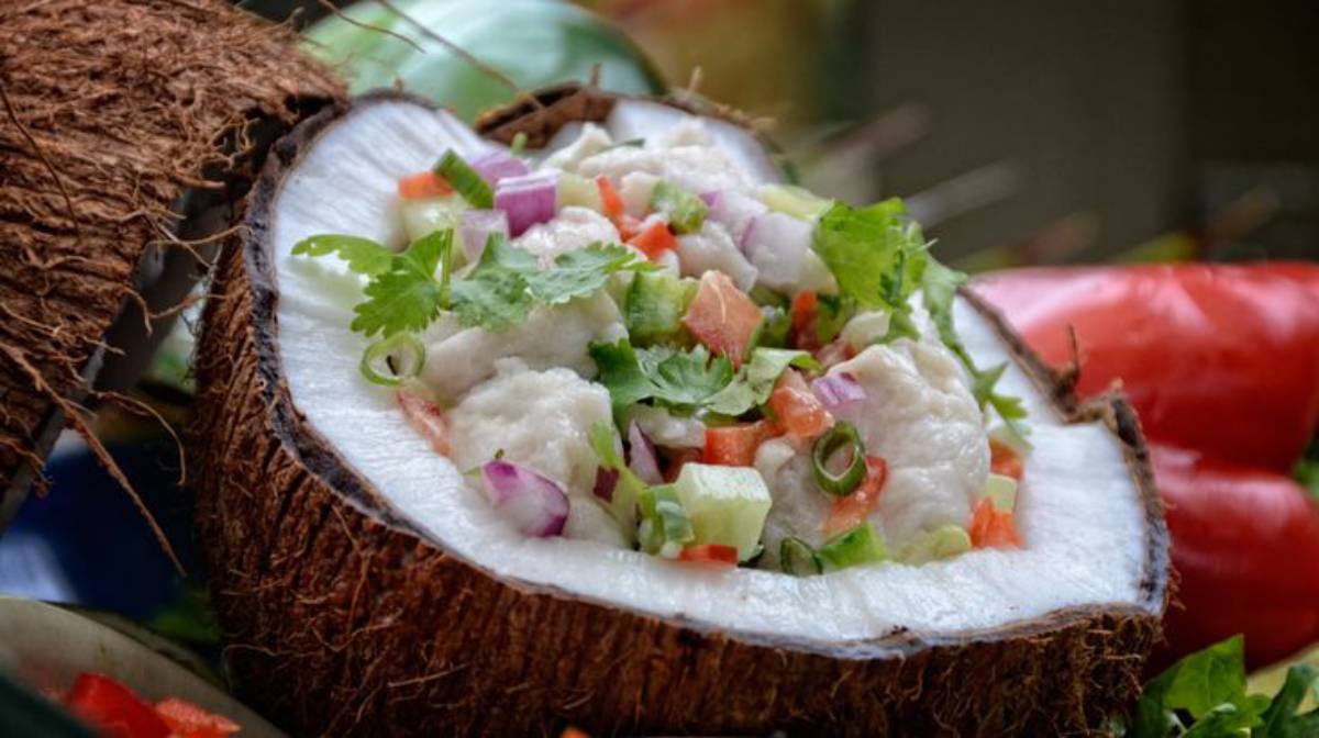 Fresh ceviche garnished with colorful vegetables served inside a halved coconut, highlighting vibrant greens and reds.