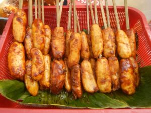 A basket filled with skewered, caramelized banana fritters on banana leaves, showcasing their golden, crispy texture.