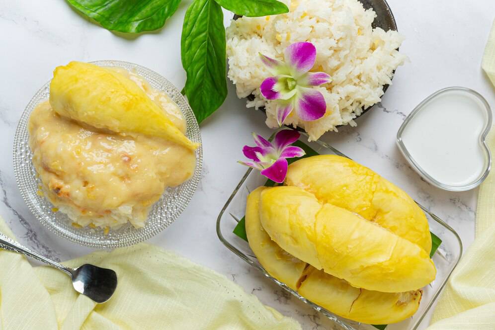A top view of sticky rice topped with sweet durian sauce, a side of fresh durian, and rice garnished with an orchid blossom.