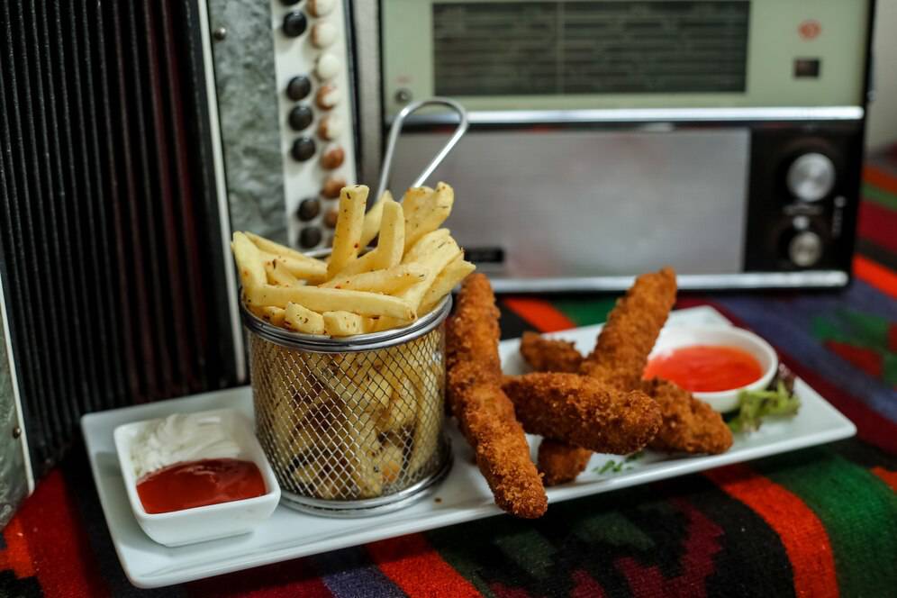 A plate with crispy fries in a metal basket dipping sauces, with a retro radio in the background.