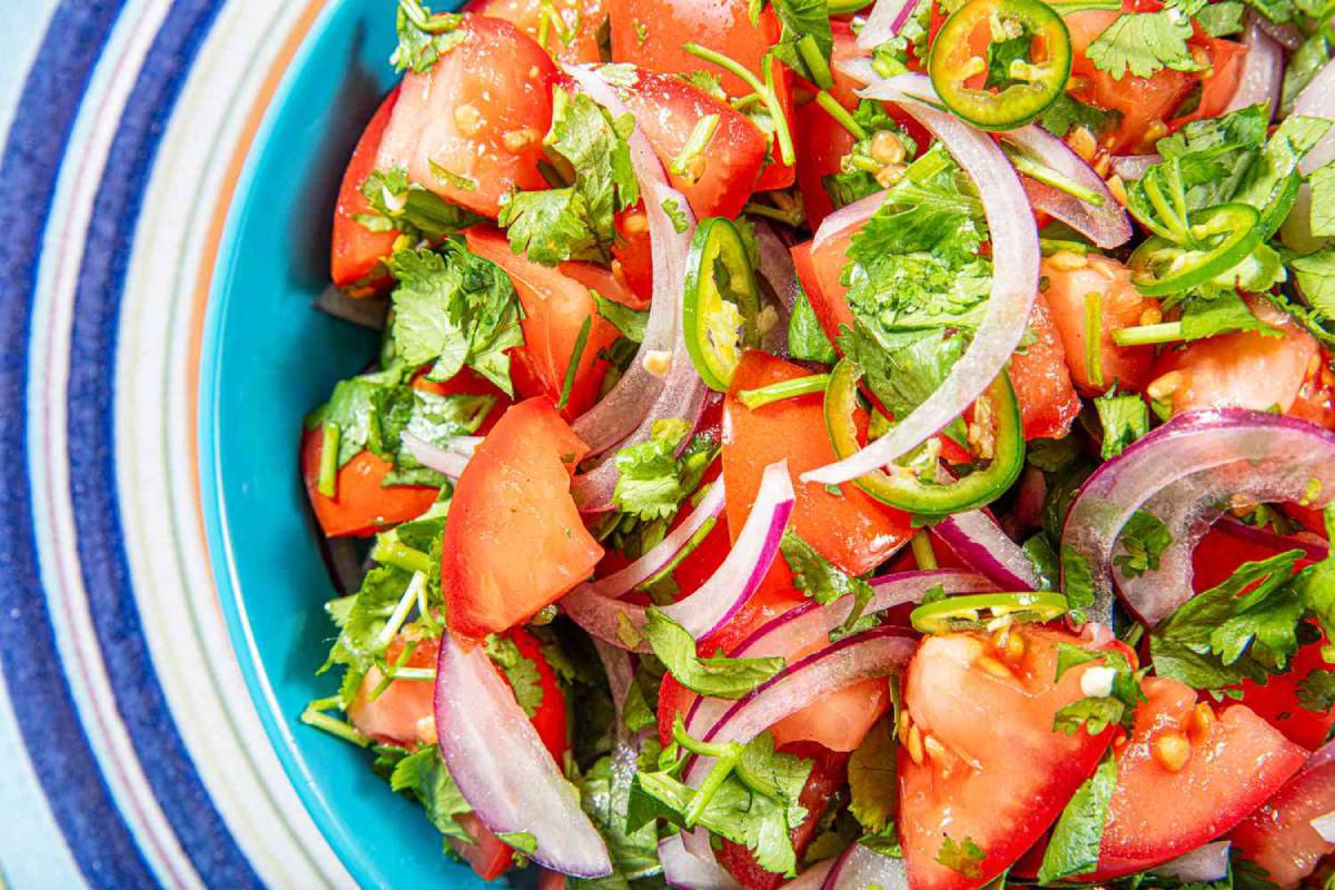A colorful salad featuring diced tomatoes, red onion, cilantro, and sliced jalapeños in a vibrant turquoise bowl.
