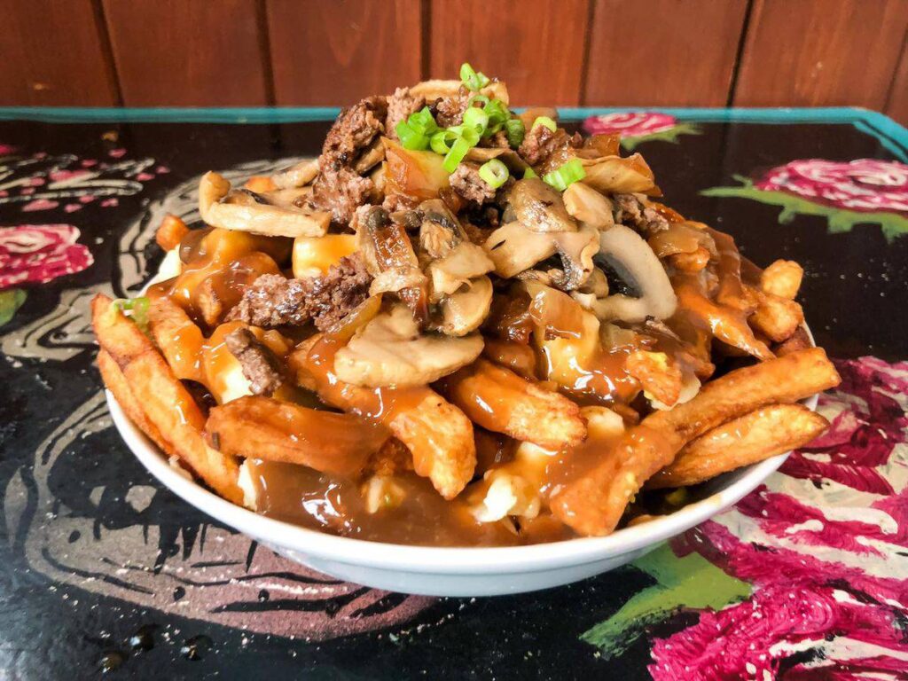 A bowl of loaded fries topped with sautéed mushrooms, beef, and smothered in gravy, served on a colorful floral tablecloth.