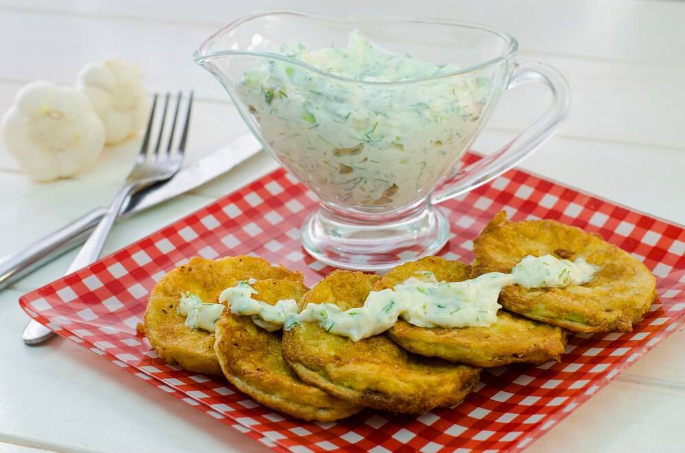 Crispy golden fritters drizzled with creamy sauce, served with a bowl of coleslaw on a red and white checkered plate.