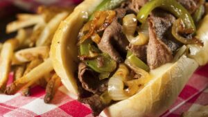 A flavorful Philly cheesesteak loaded with sautéed onions and green peppers, beside a serving of crispy French fries.