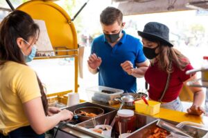 A vibrant street food stall with a vendor serving a couple, showcasing an assortment of colorful dishes and condiments.