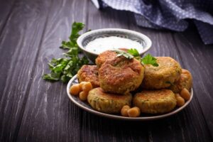 A close-up of a plate of golden-brown meat patties garnished with fresh parsley and green onions, surrounded by cloves of garlic.