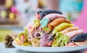 A vibrant stack of colorful rolled desserts featuring shades of pink, green, yellow, and black, showcasing a sweet, layered treat.